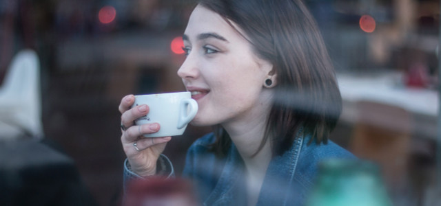 A young woman with a brown bob sips coffee from a white porcelain mug
